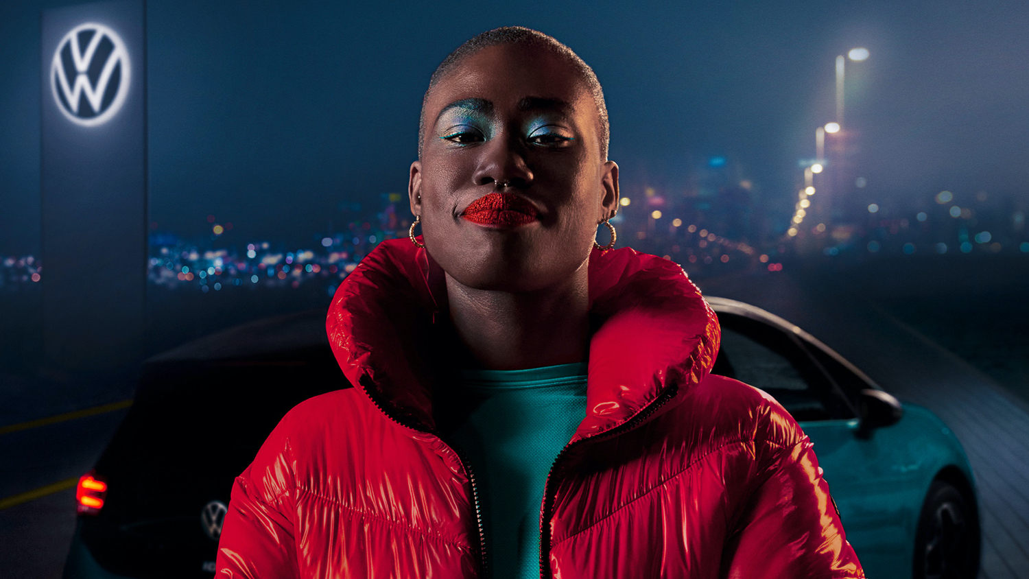 Een vrouw in een rode jas die voor een VW ID. staat met een verlicht VW-logo in de achtergrond