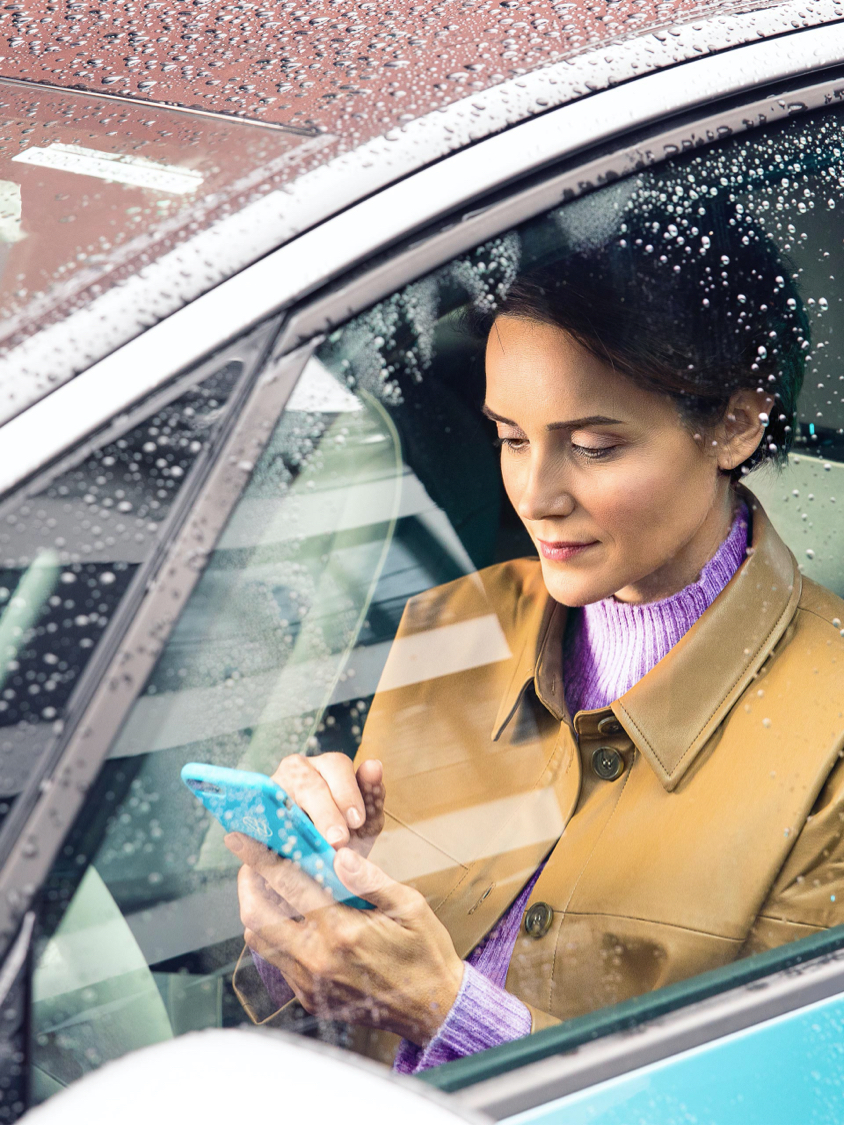 Een vrouw zit in haar VW ID. en typt iets in haar mobiele telefoon – VW Over-the-Air update