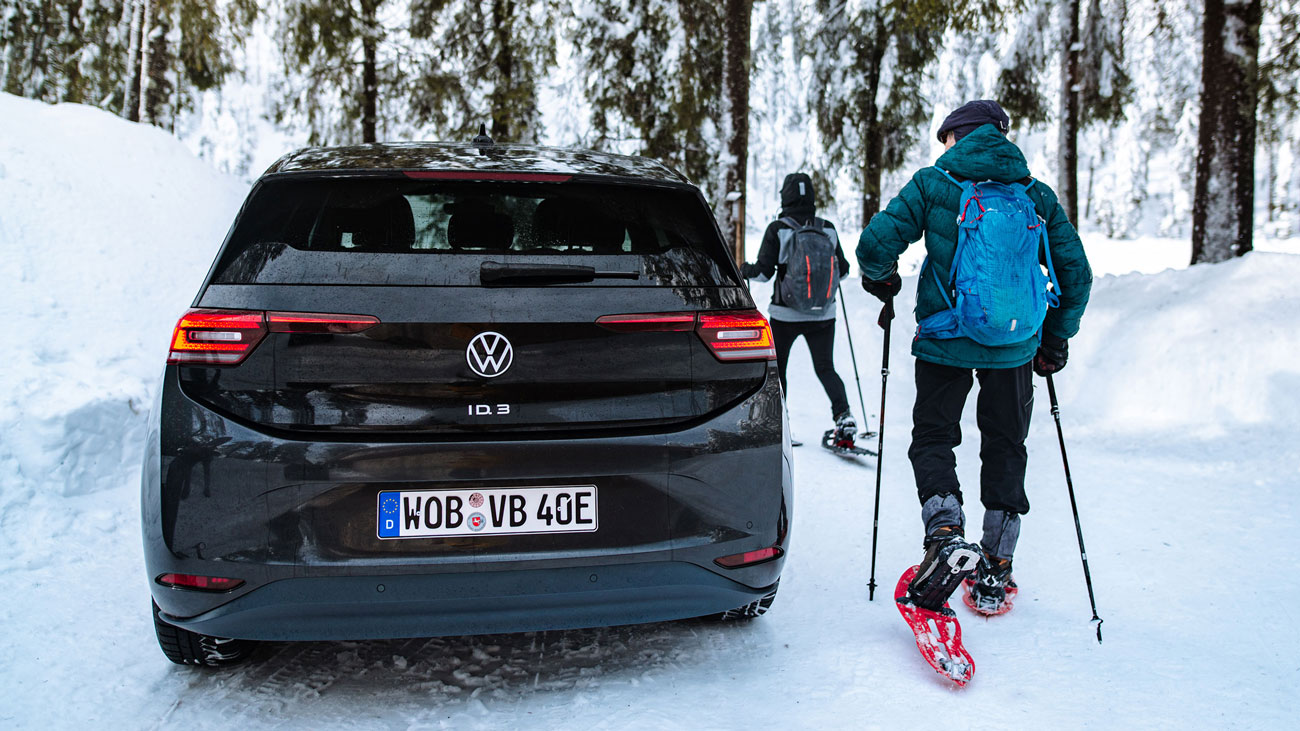 Een zwarte VW ID.3 in een bosrijk sneeuwlandschap met twee skiërs